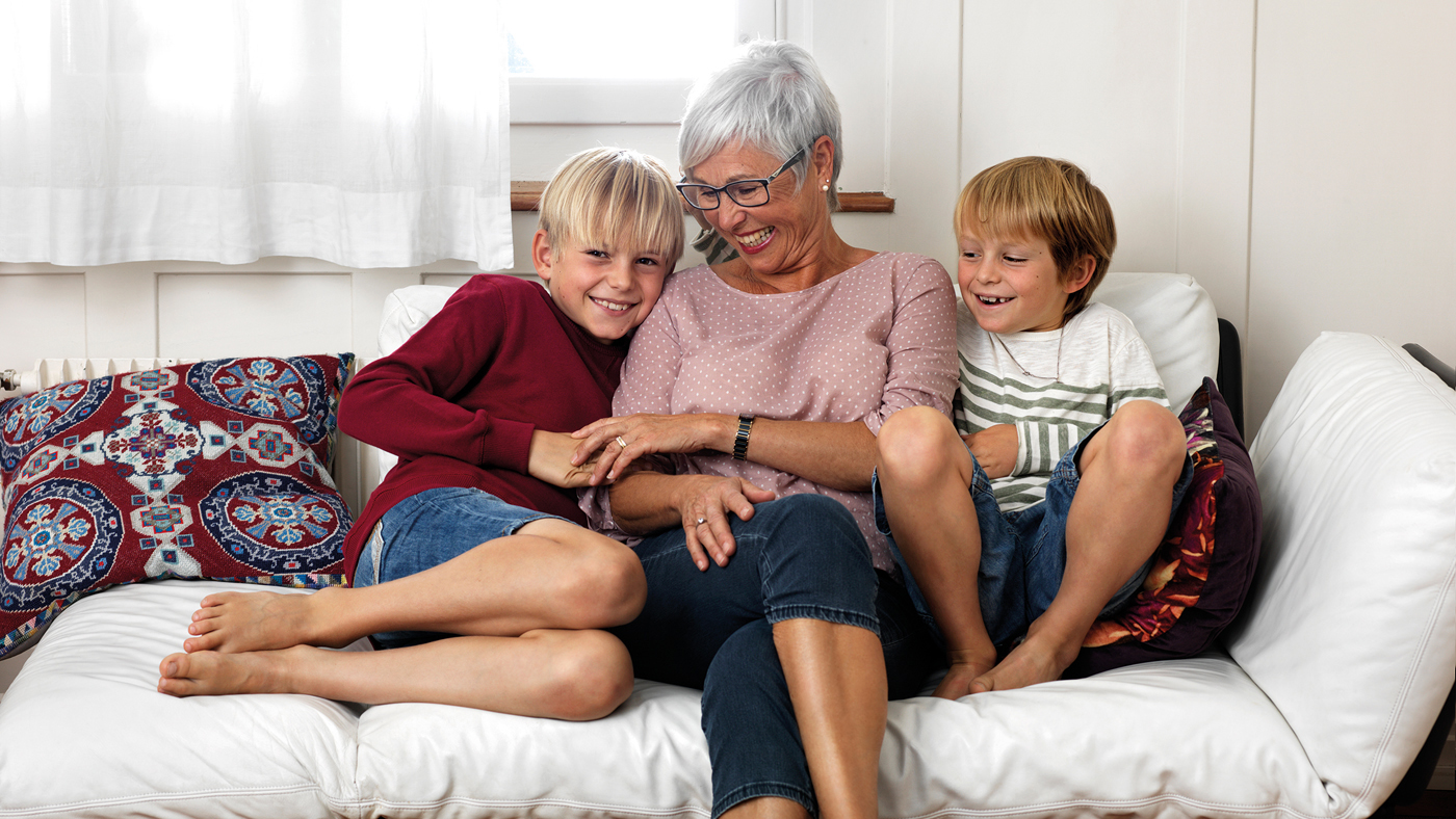 Eine Seniorin sitzt mit ihren Enkeln auf dem Sofa und lacht